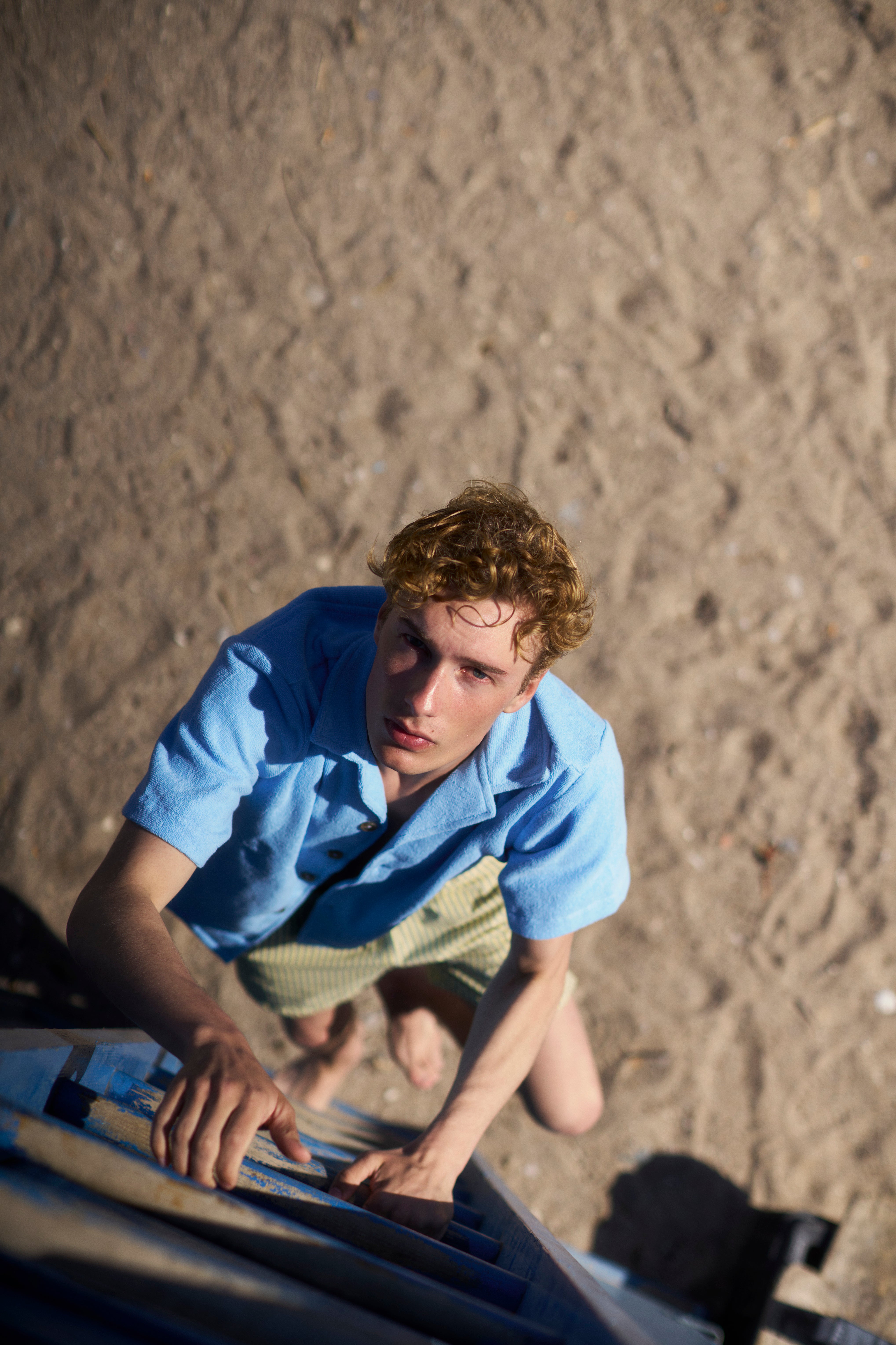 Man in a Coastal Blue organic cotton terry camp-collar shirt, climbing a ladder on a beach