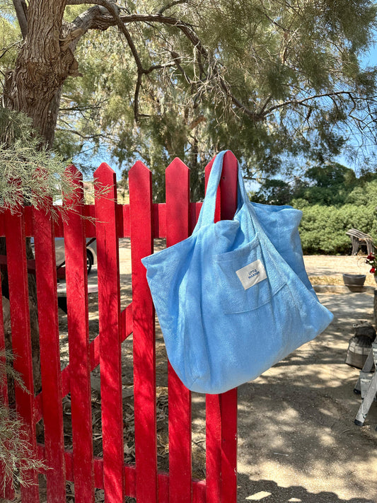 Little Mariner coastal blue bag hanging on a red wooden fence with trees and a person in the background