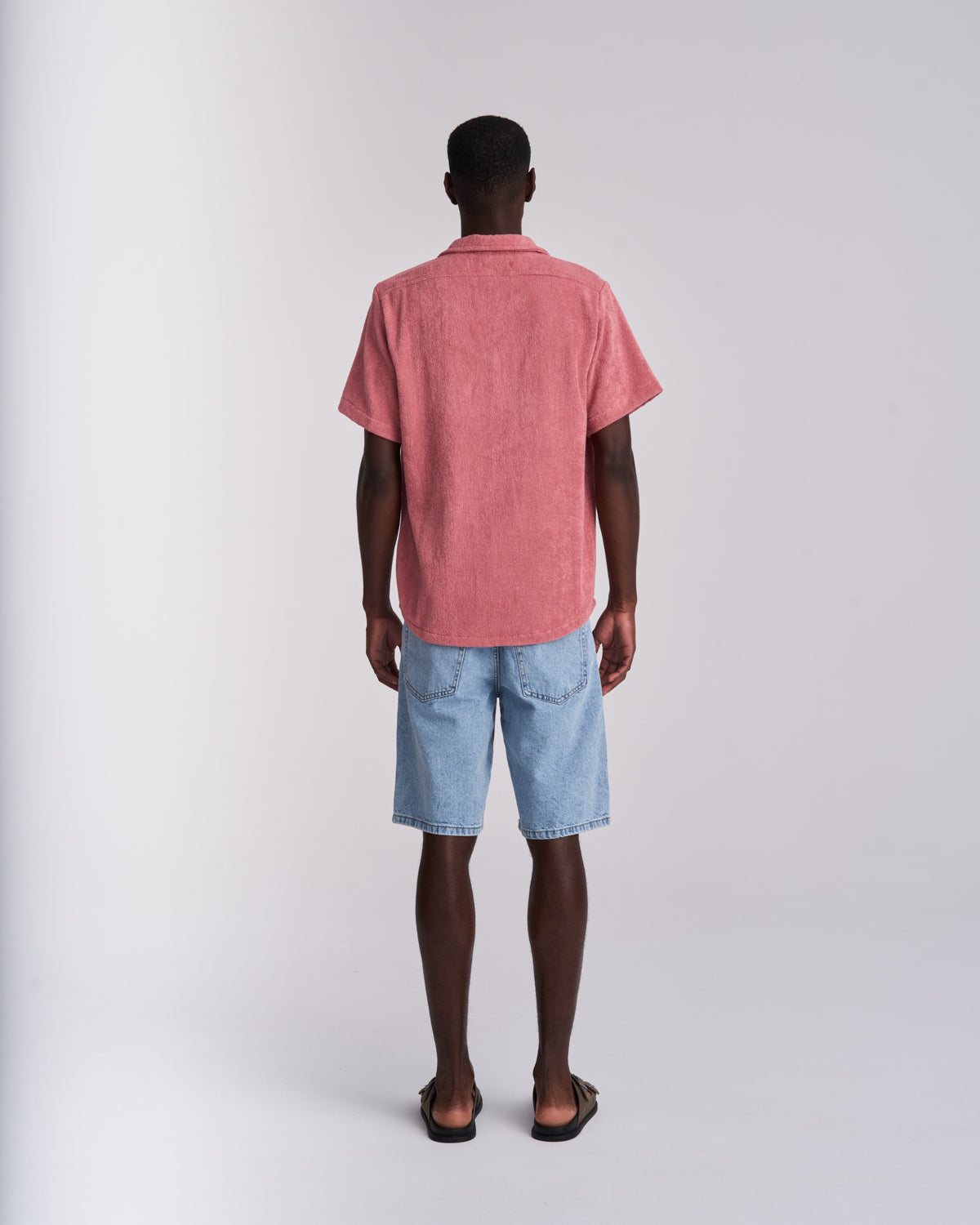 Back view of a man wearing a Dusty Rose organic cotton terry camp-collar shirt styled with jean shorts