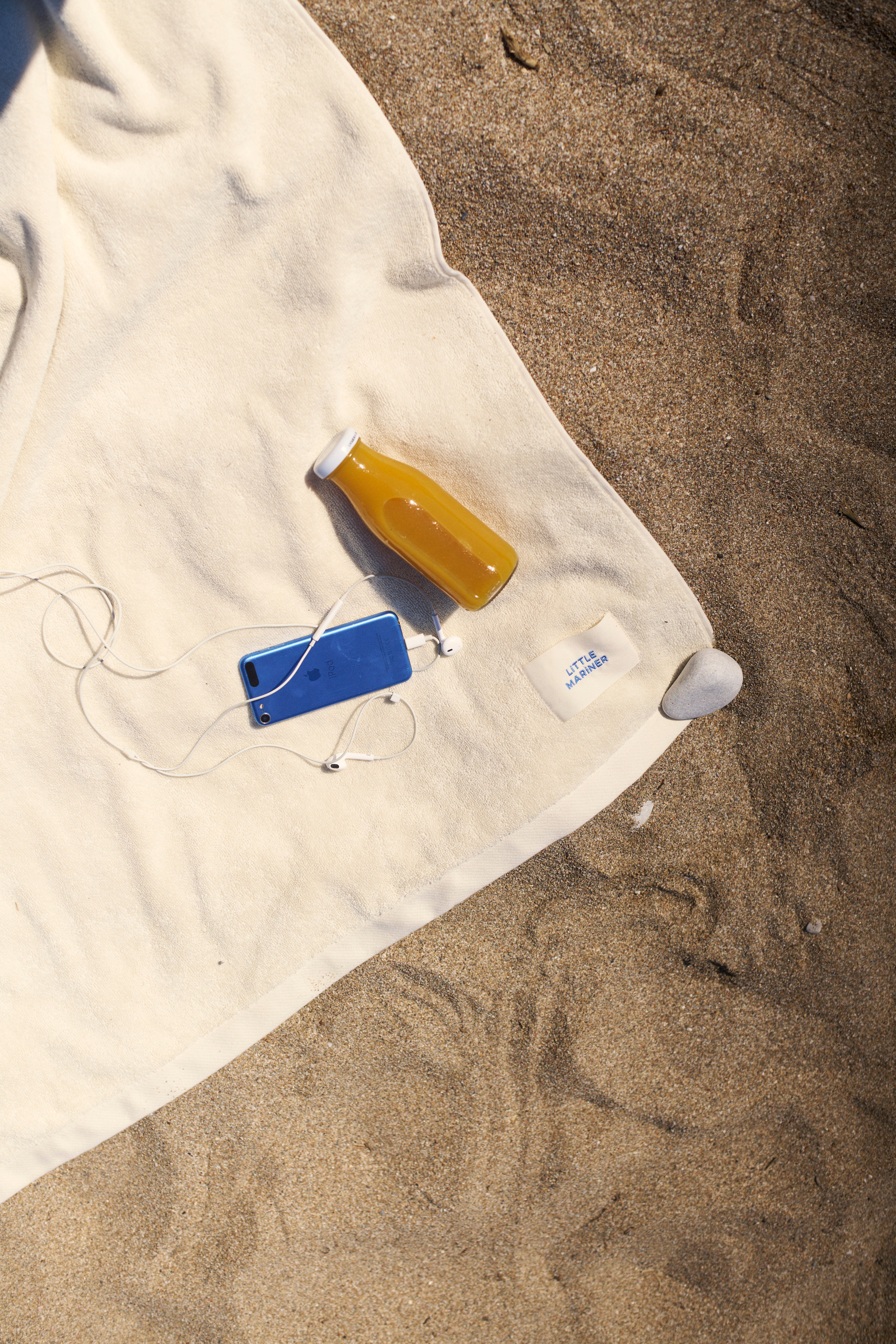 Off-White organic cotton terry towel spread on a sandy beach with a woven LiTTLE MARiNER label
