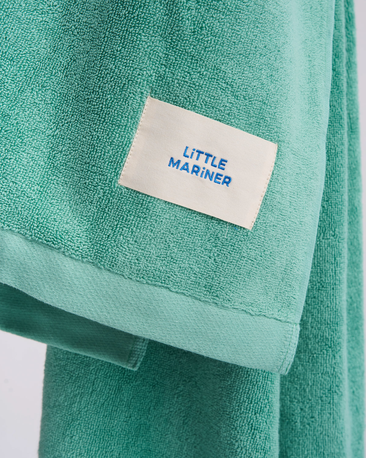 Close-up of the woven LiTTLE MARiNER label on a Sage Green organic cotton terry towel