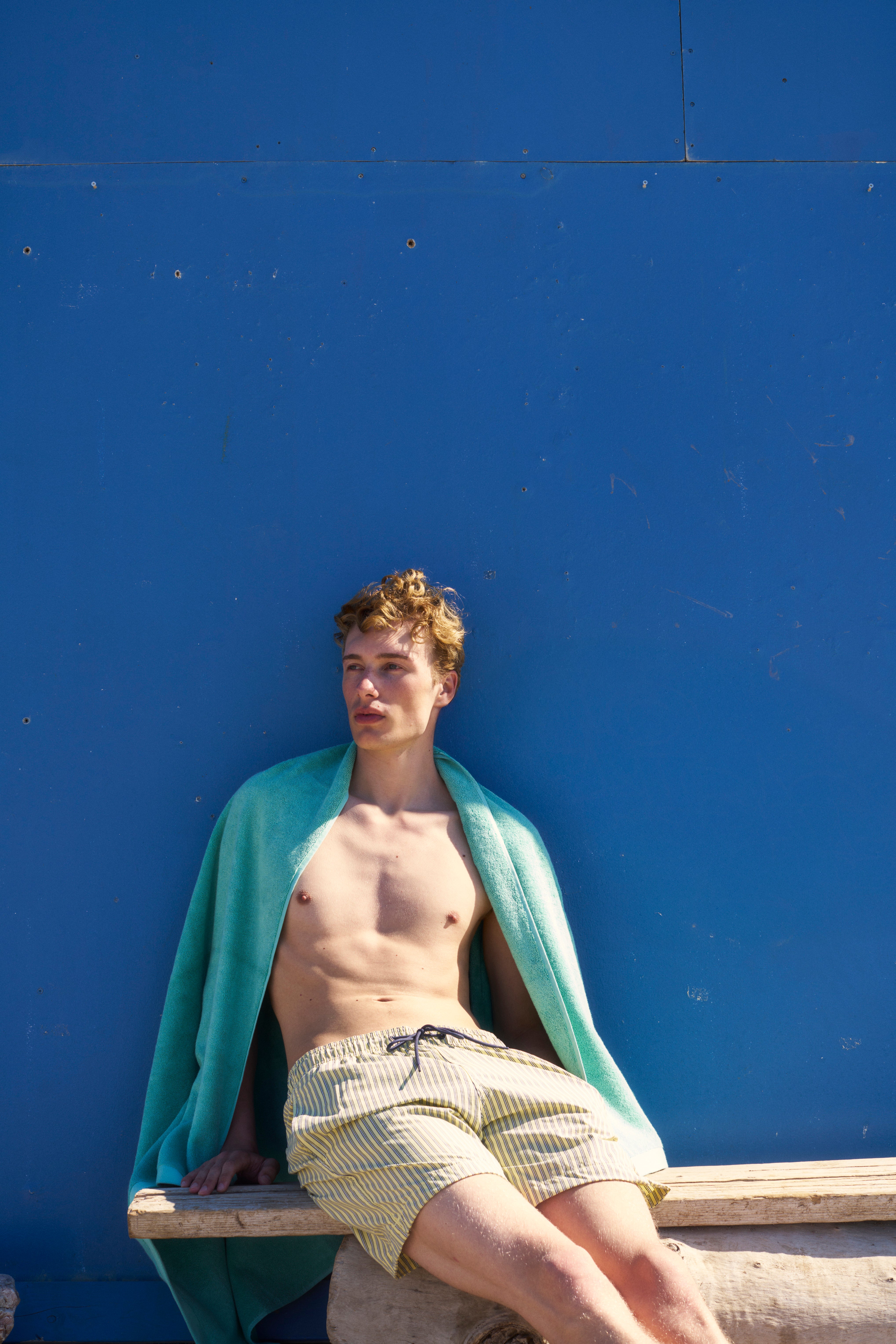 Man against a blue wall with a Sage Green organic cotton terry towel over his shoulders
