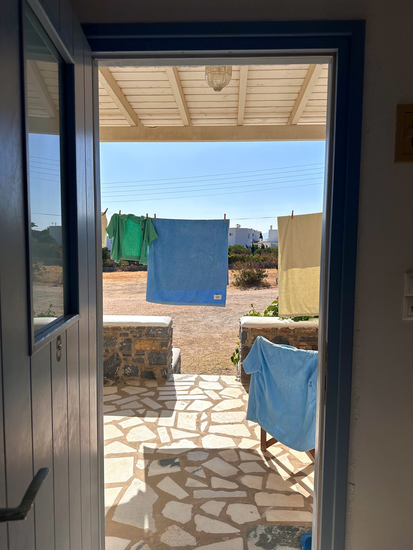 View from a door into an outdoor area with Little Mariner coastal blue towel and terry clothes hanging on a line.