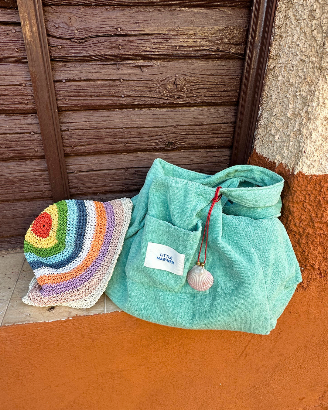 #Sage Green Little Mariner terry bag with a pink seashell charm from Sunday Jewellery, next to a rainbow crochet hat.