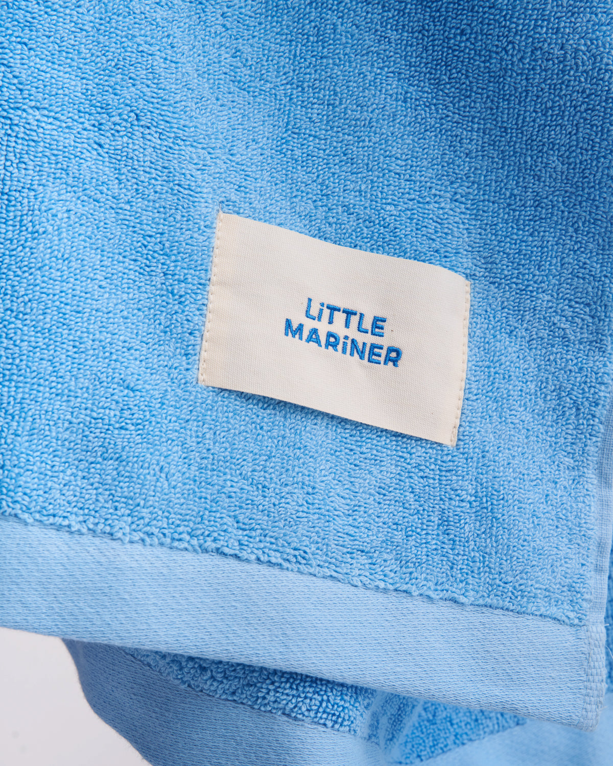 Close-up of the woven LiTTLE MARiNER label on a Coastal Blue organic cotton terry towel