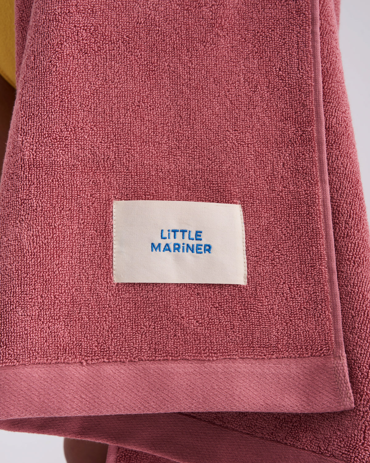 Close-up of the woven LiTTLE MARiNER label on a Dusty Rose organic cotton terry towel