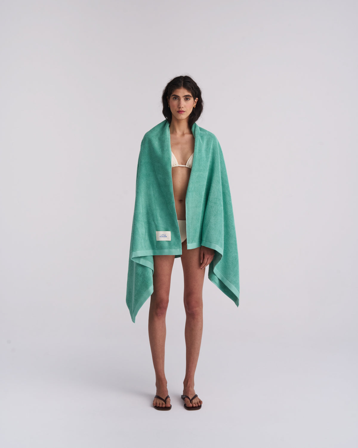 Woman wrapped in a Sage Green organic cotton terry towel over a cream swimsuit