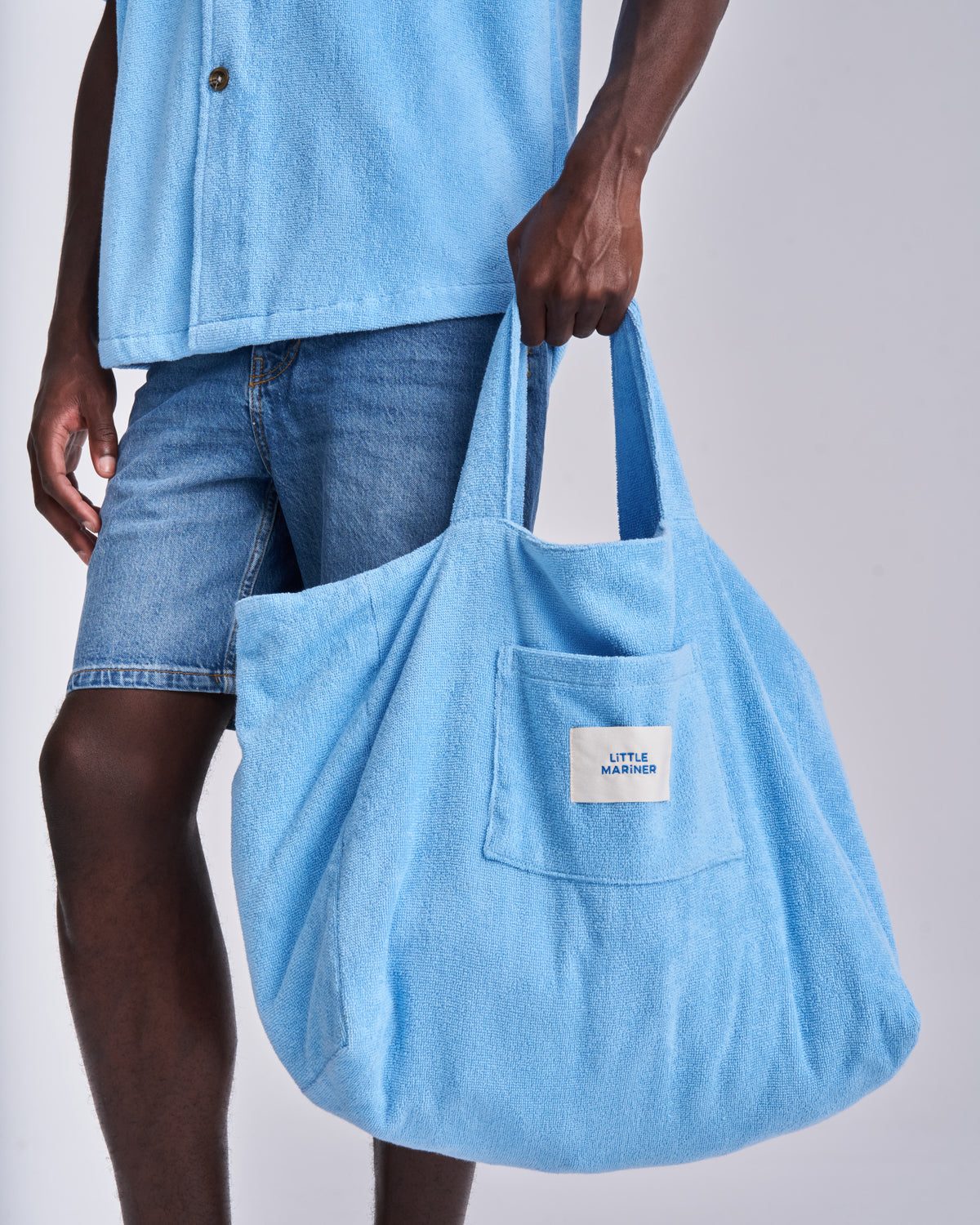 Coastal Blue organic cotton terry tote bag held by the handles, front pocket and woven label
