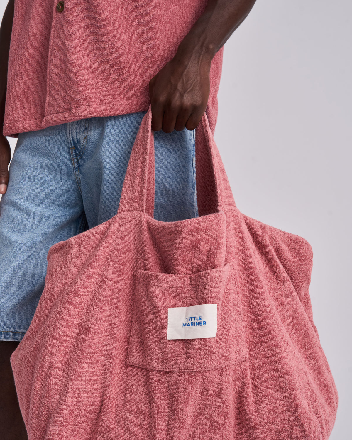 Dusty Rose organic cotton terry tote bag held by the handles, front pocket and woven label