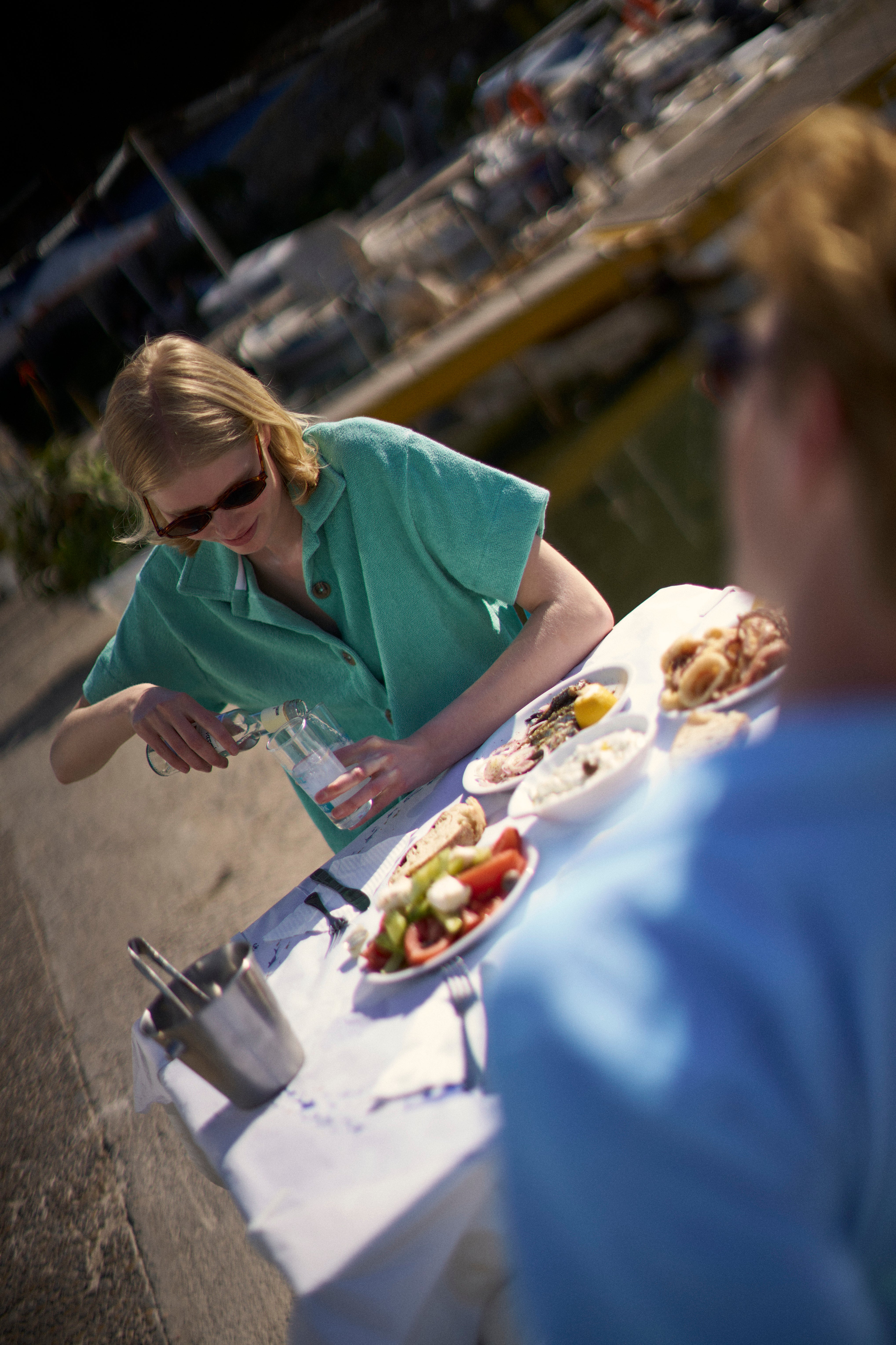Woman in a Sage Green organic cotton terry camp-collar shirt at a harbourside taverna table