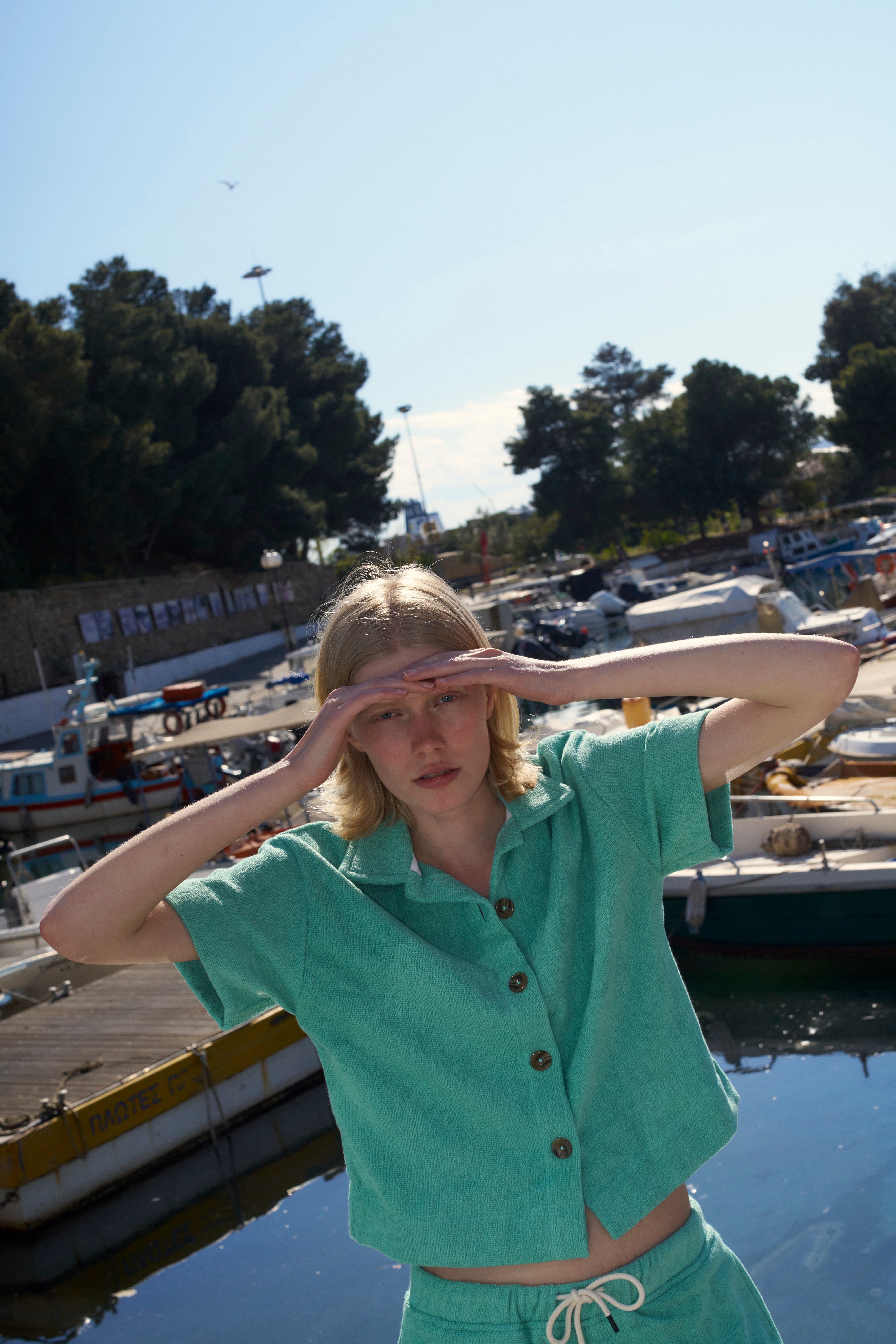 Woman in a Sage Green organic cotton terry camp-collar shirt and matching shorts by a harbour