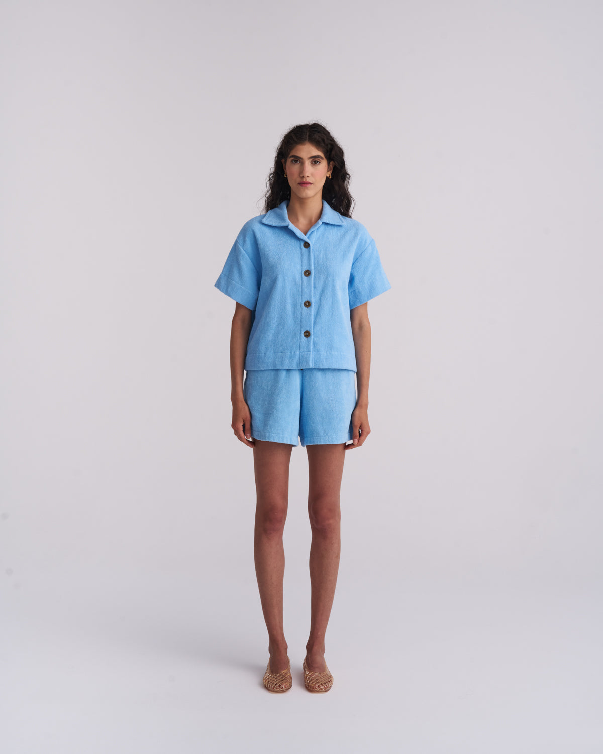 Woman in a Coastal Blue organic cotton terry camp-collar shirt and matching terry shorts, front view