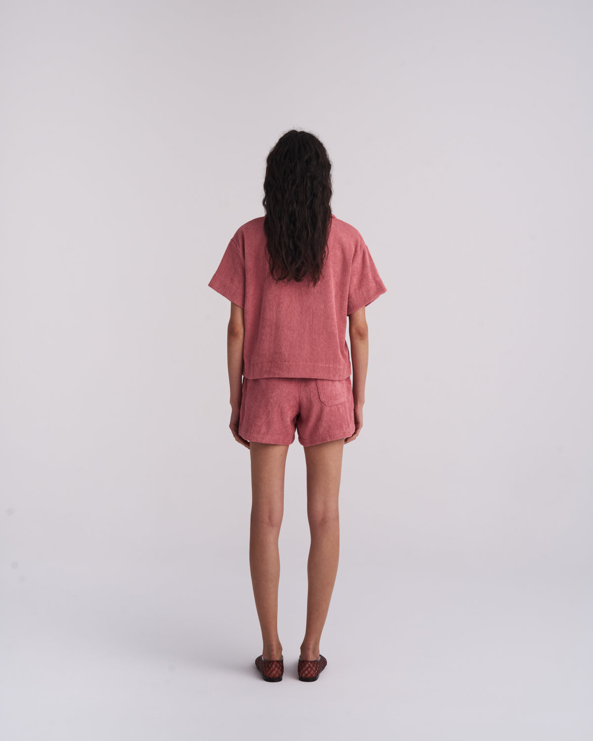 Woman in a Dusty Rose organic cotton terry camp-collar shirt and matching terry shorts, back view